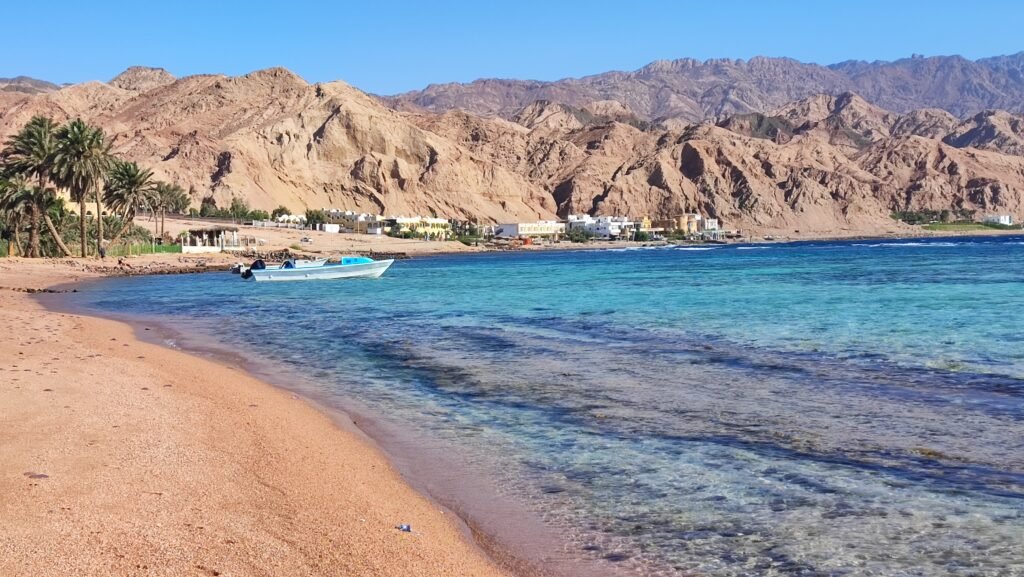 Scenic beach in Dahab, Egypt with clear waters, palm trees, and mountains-ideal for a two-week travel itinerary.